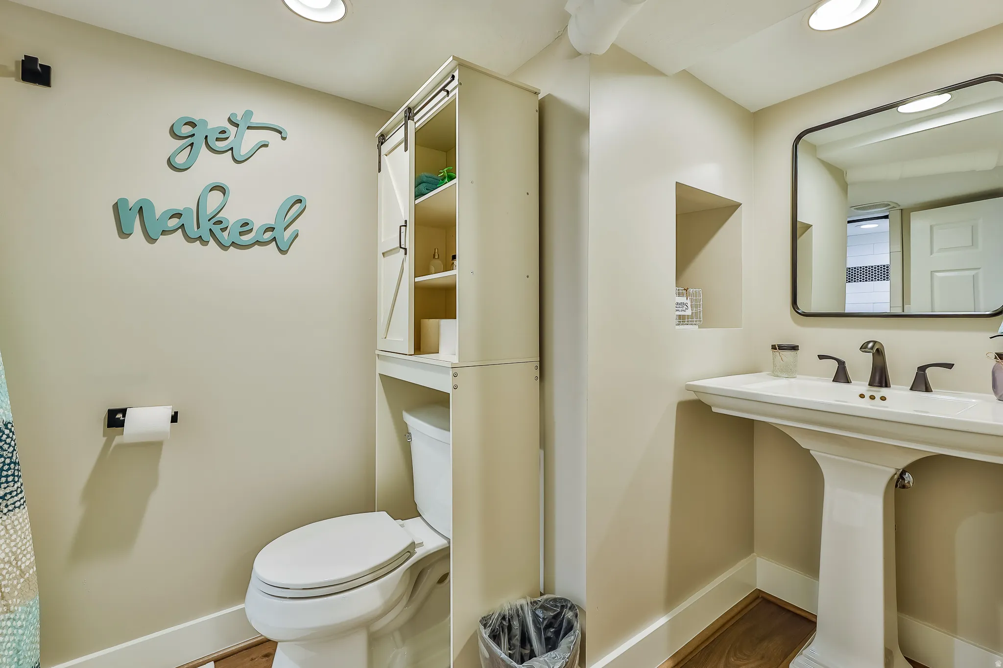 Pedestal sink with black-framed mirror, integrated wall niche, recessed lighting, and wood-finish flooring
