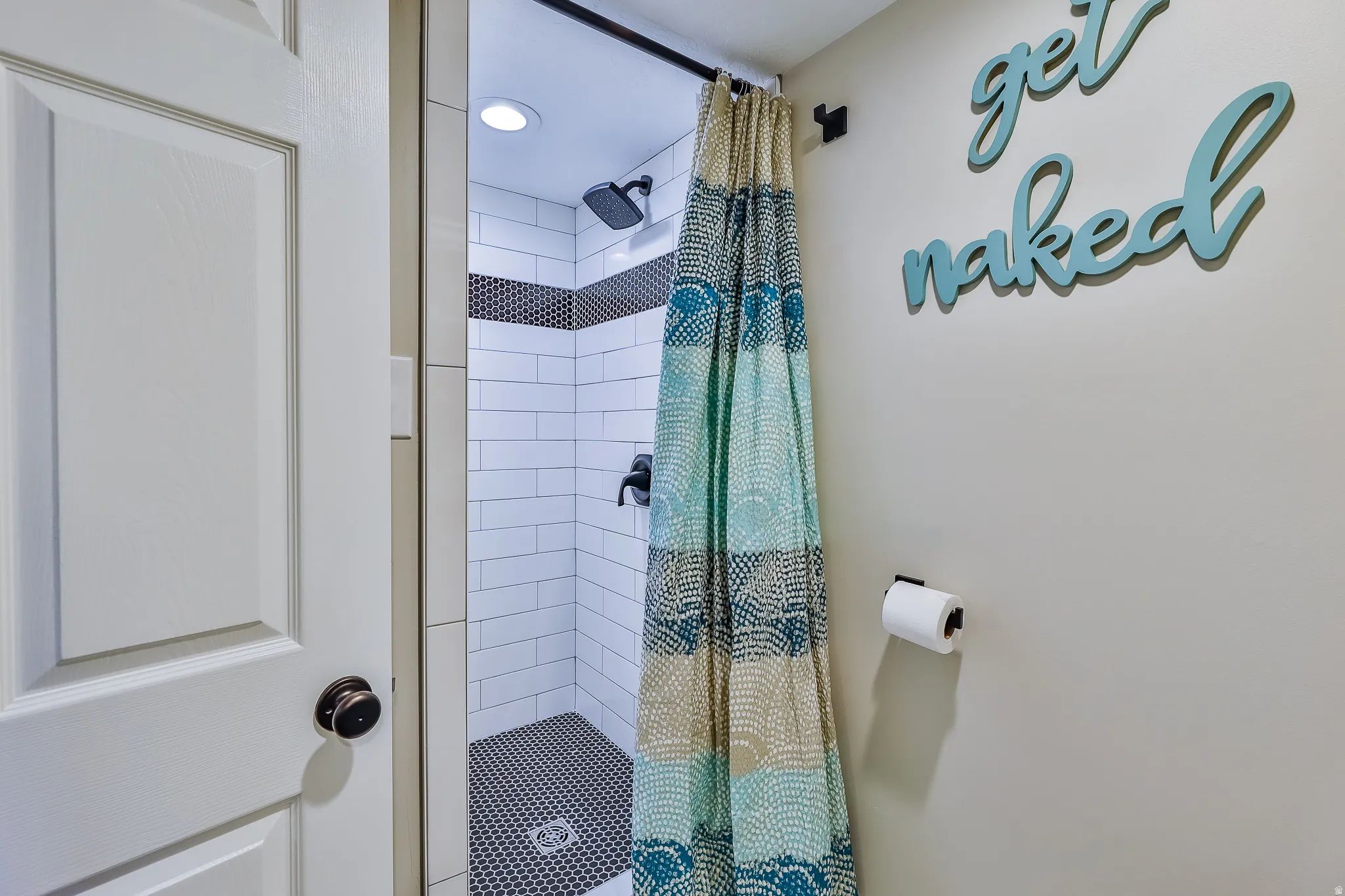 Shower featuring white subway tile, a dark accent tile band, and dark hexagonal floor tiles