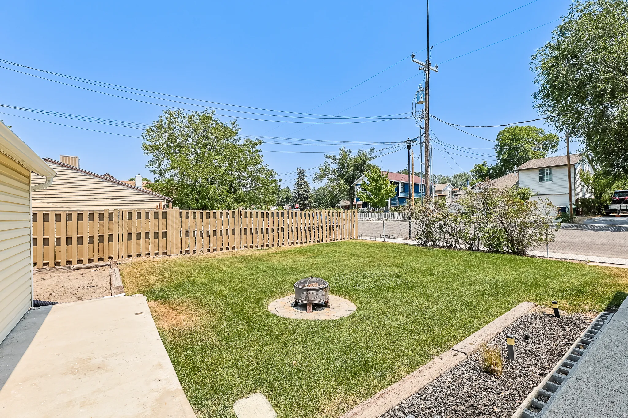Fenced backyard with a central fire pit, concrete patio, and a landscaped border