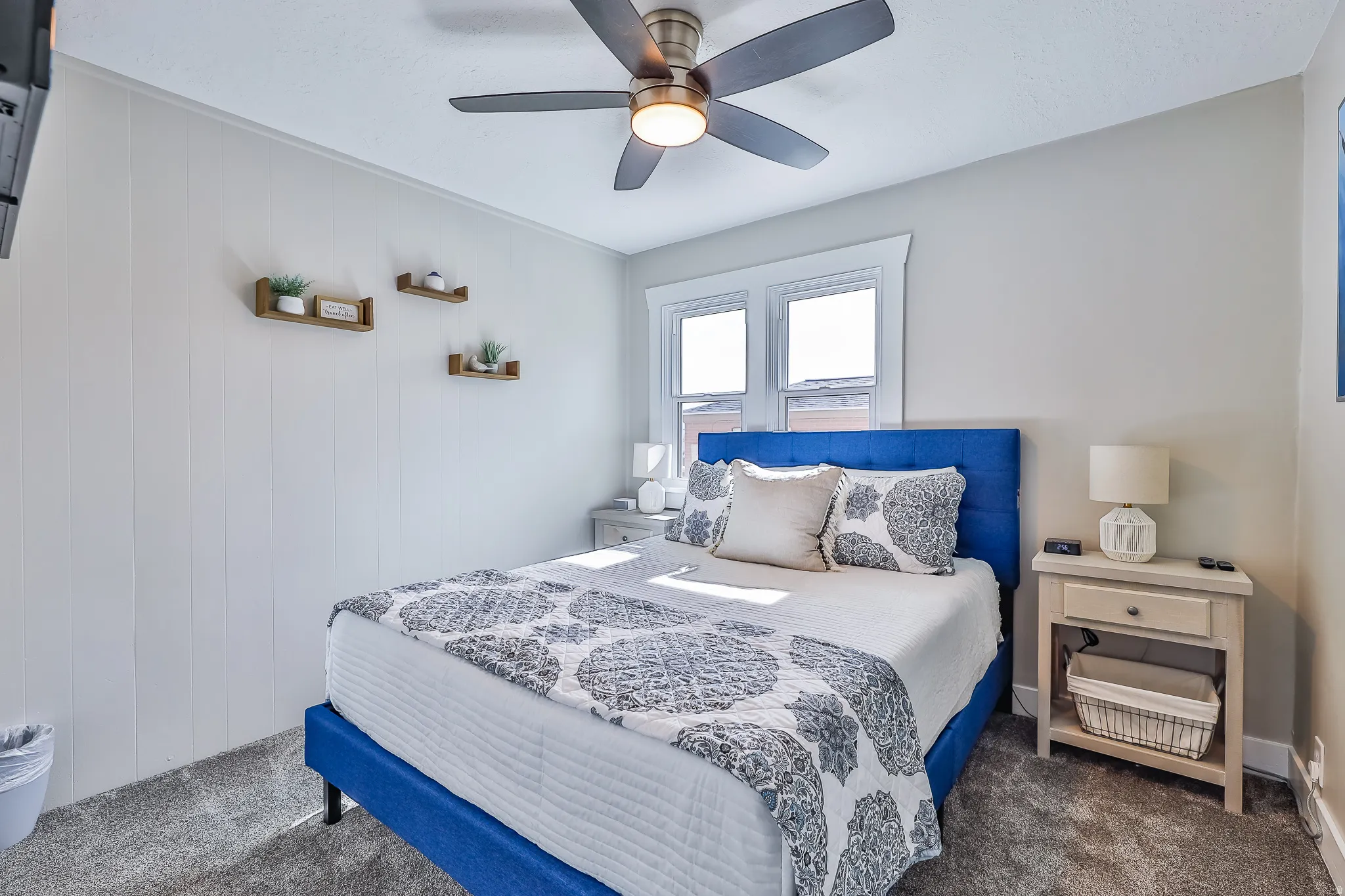 Bright interior space featuring a window with white trim, a ceiling fan with integrated lighting, and light-colored wall paneling