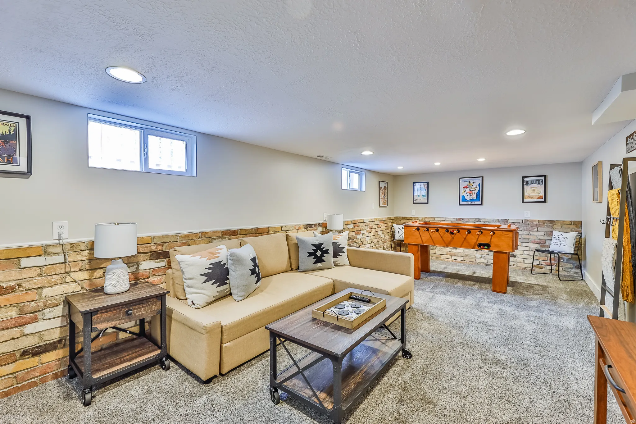 Spacious recreation room featuring carpet flooring, recessed lighting, and a brick accent wall
