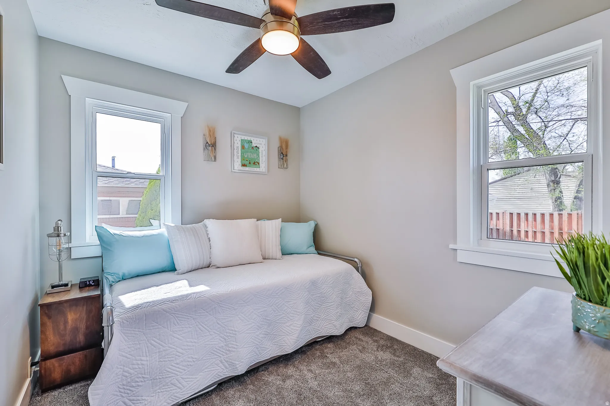 Carpeted room with a ceiling fan, two windows, and neutral wall paint