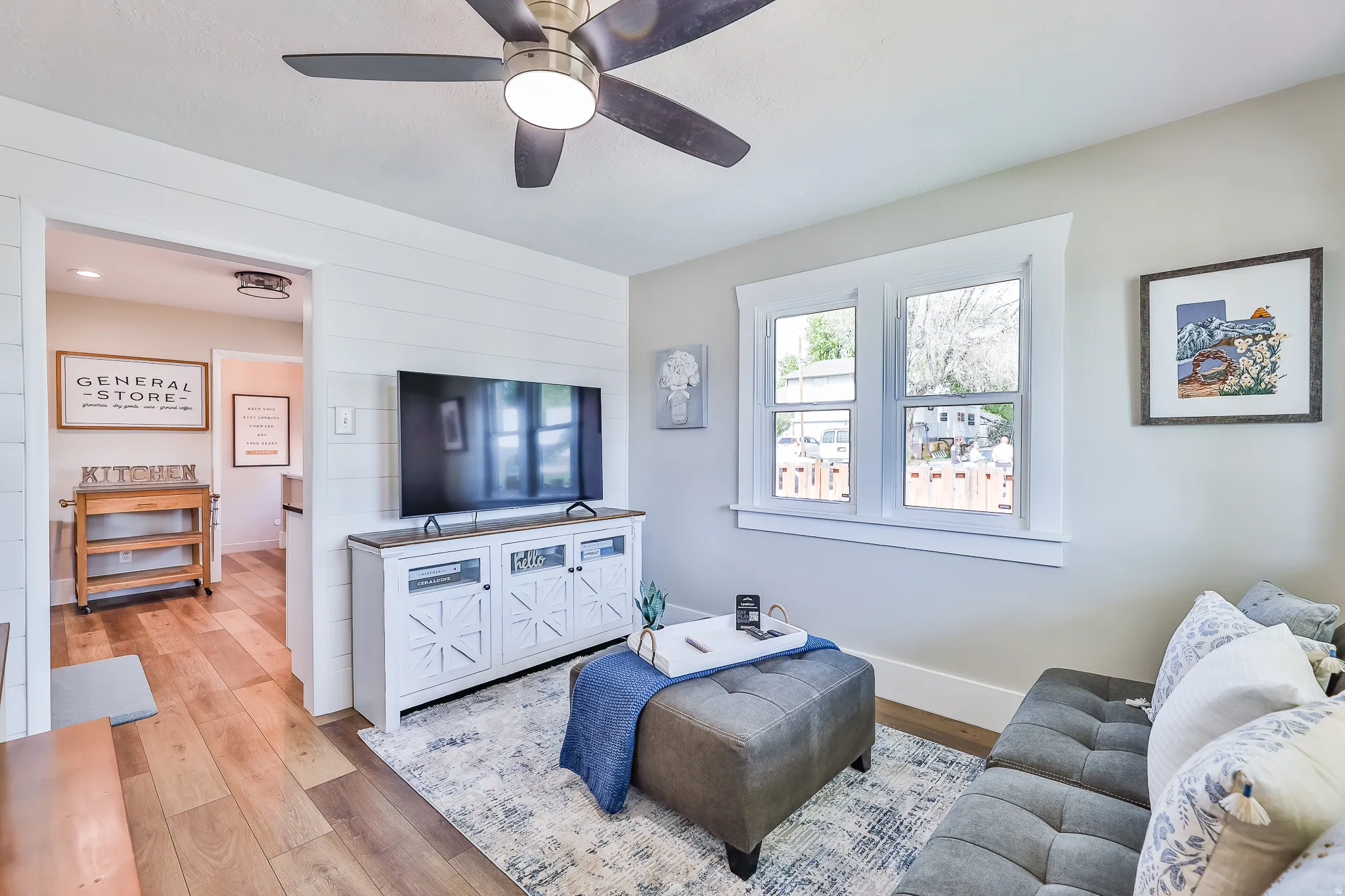 Open concept living area featuring wood-finish flooring, a ceiling fan with integrated lighting, and white shiplap accent wall paneling