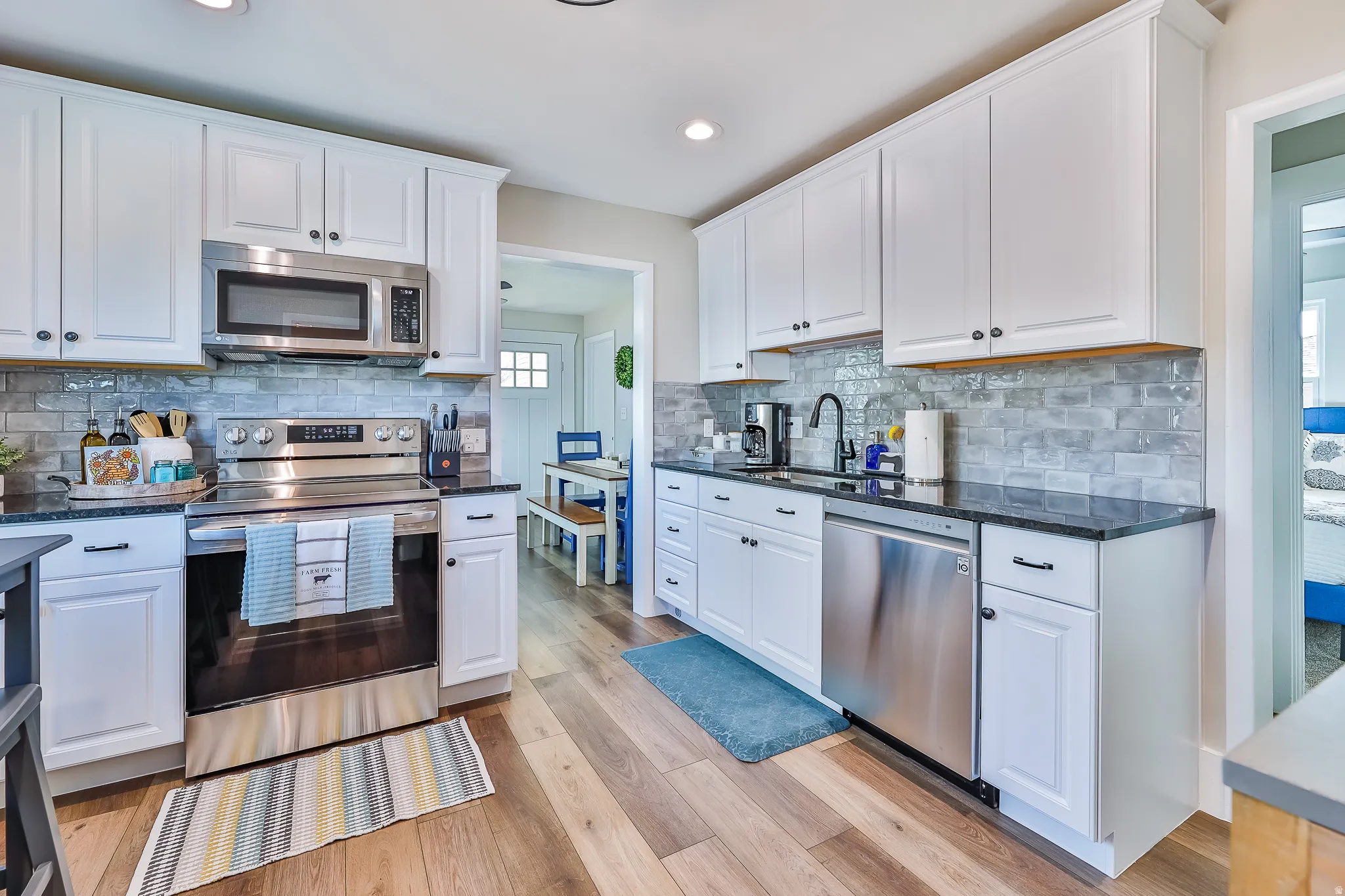 Kitchen featuring white cabinetry, dark countertops, wood-finish flooring, stainless steel appliances, and a subway tile backsplash