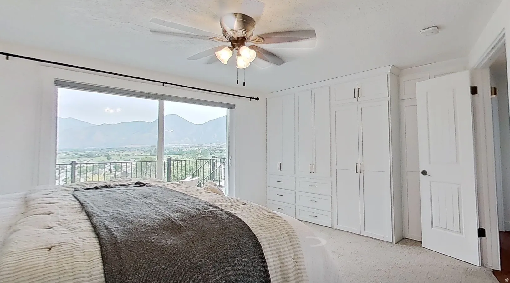 Room featuring a sliding glass door, a balcony with metal railings, a ceiling fan, white built-in cabinetry with silver-tone hardware, and light-toned carpet flooring