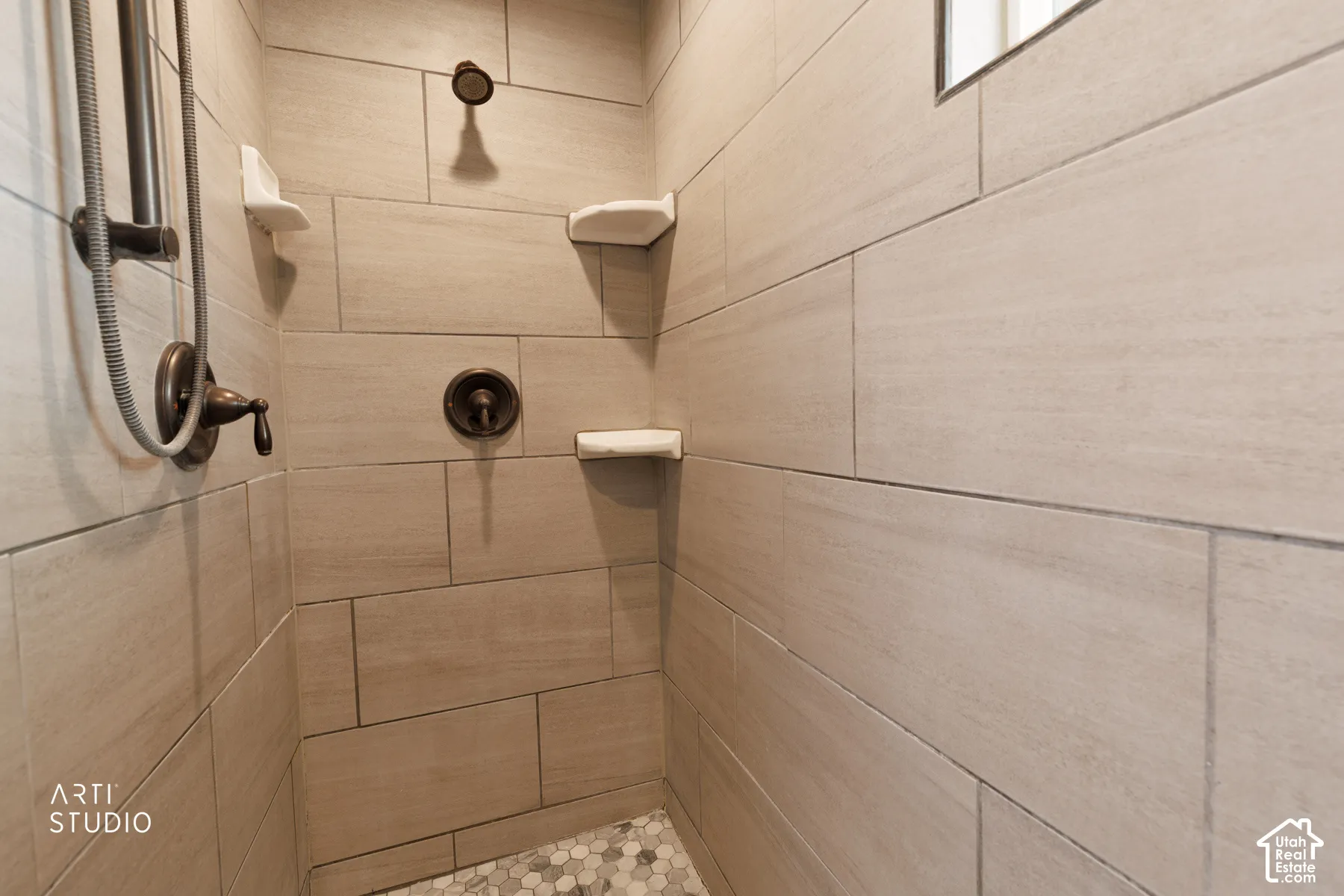 Shower stall featuring large format rectangular wall tiles, a mosaic tile floor, and oil-rubbed bronze fixtures, including a handheld showerhead