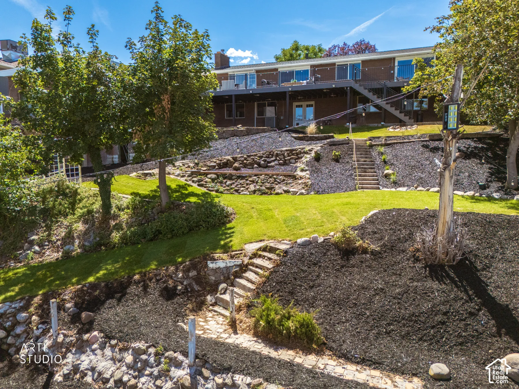 Multi-level backyard with tiered landscaping, manicured lawn, stone retaining walls, and a full length deck with exterior stairs