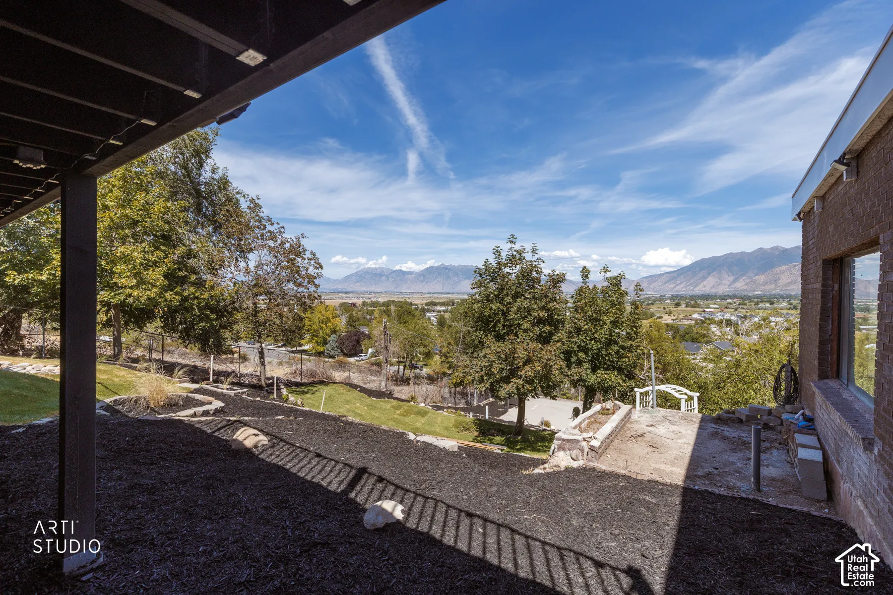 Lower-level patio space with a manicured lawn, established trees, and mountain scenery
