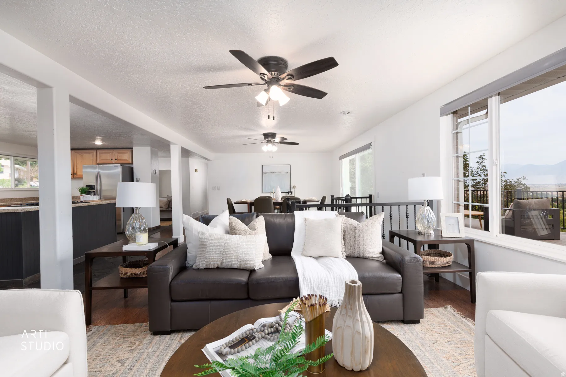 Living area with wood-finish flooring, two ceiling fans, and a large window overlooking an outdoor deck