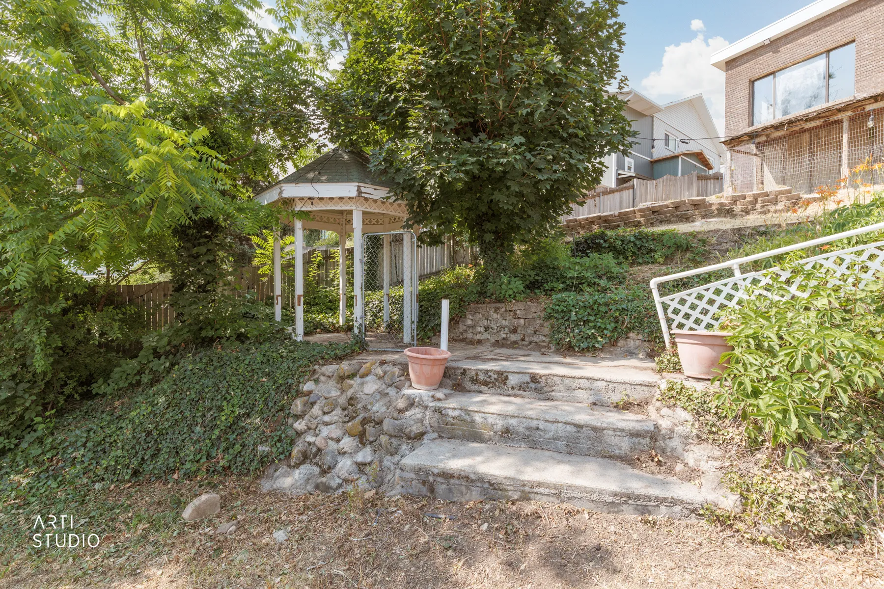 Backyard features a white gazebo, stone retaining walls, concrete steps, and established trees and shrubs