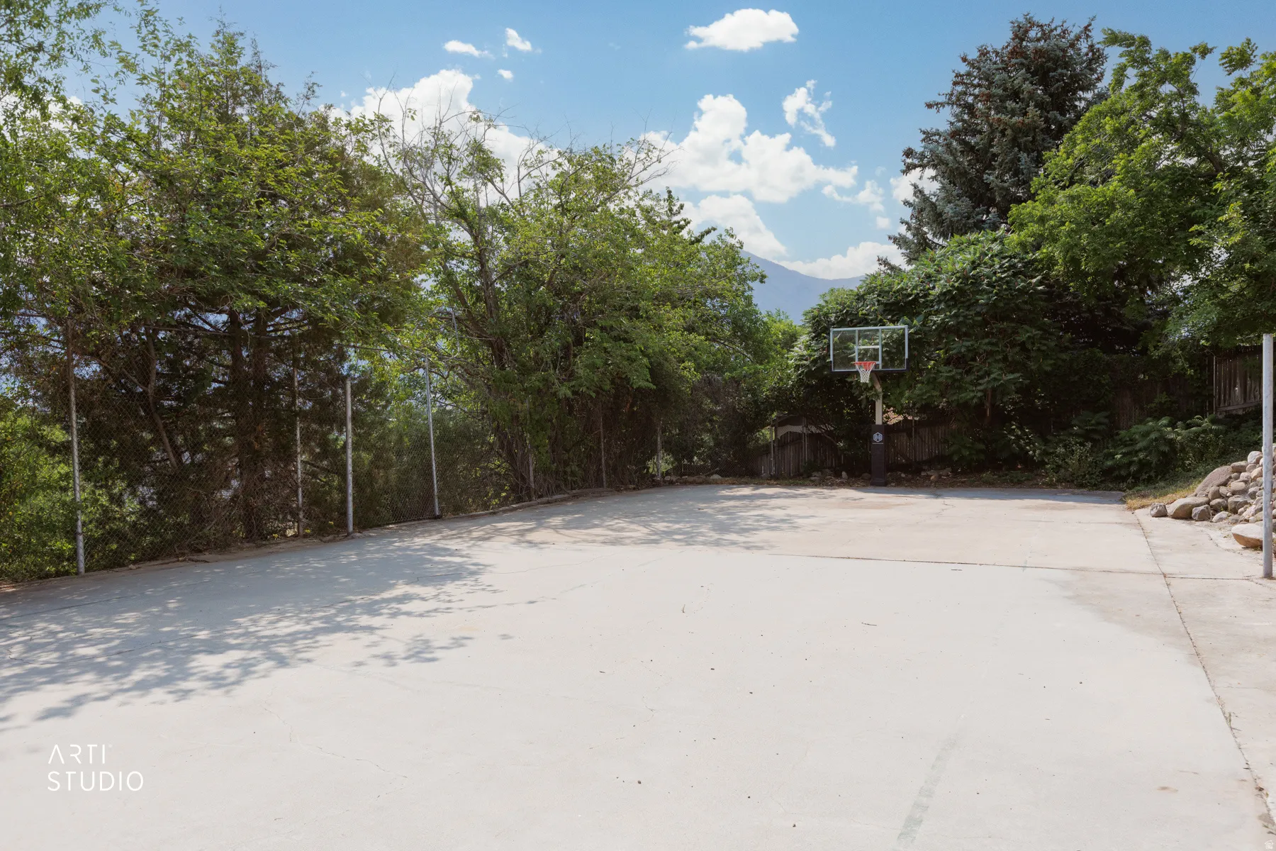 Concrete full basketball court with permanent basketball hoops, surrounded by mature trees and natural landscaping