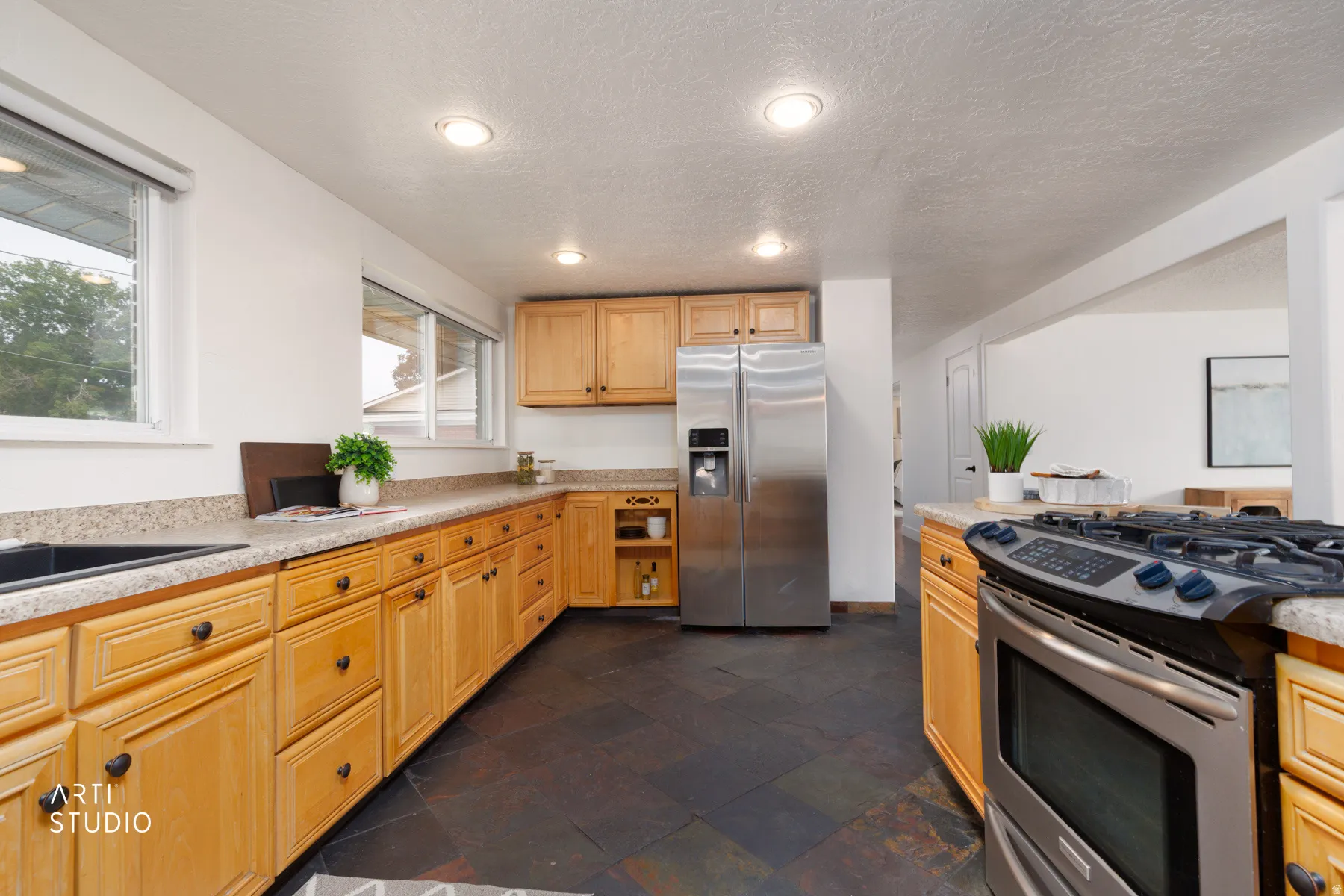 Kitchen featuring natural wood cabinetry, dark stone-finish flooring, a stainless steel side-by-side refrigerator, and a stainless steel gas range