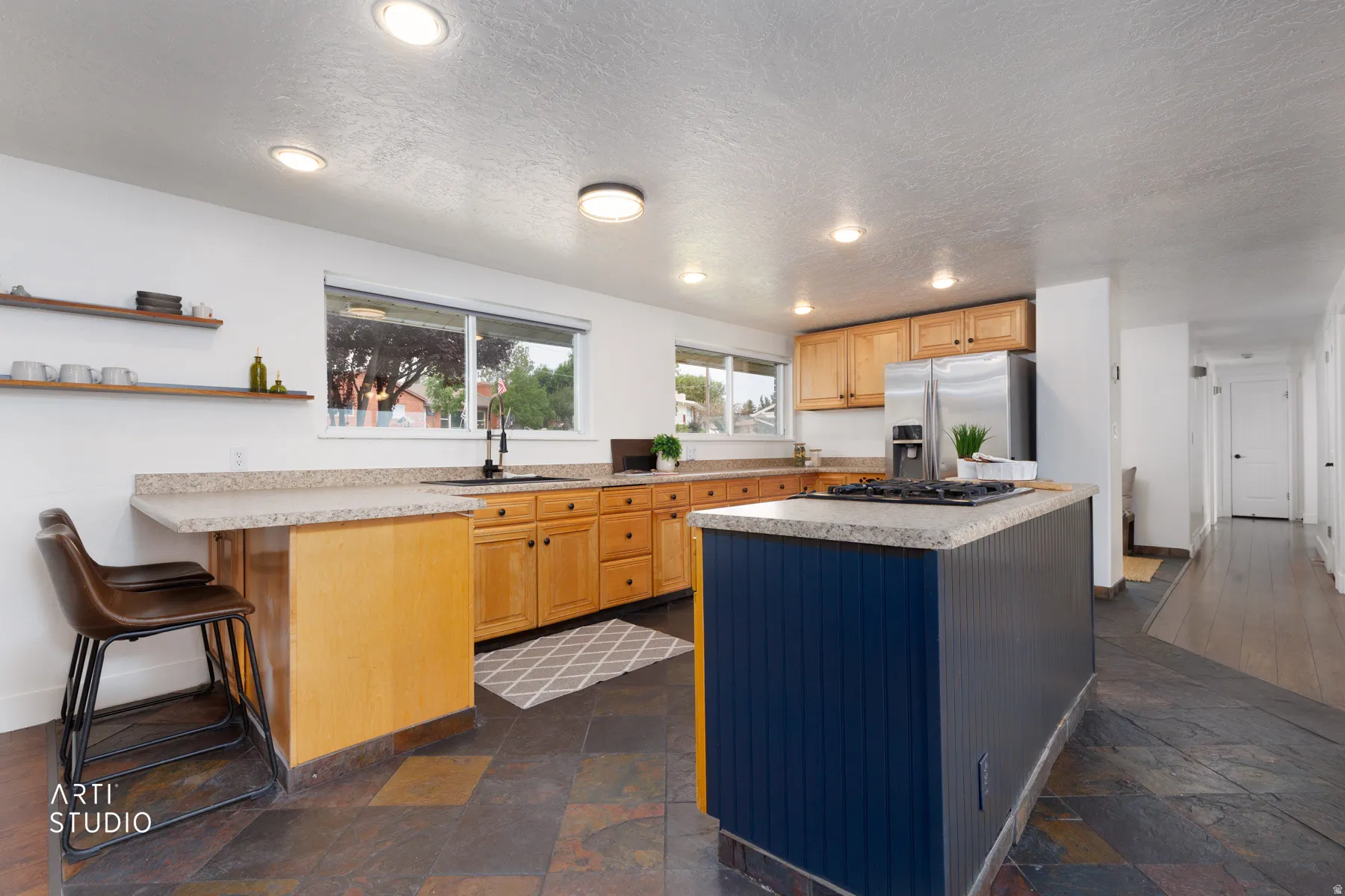 Kitchen featuring slate flooring, light wood cabinetry, a center island with a black base, stainless steel appliances, and light-colored countertops