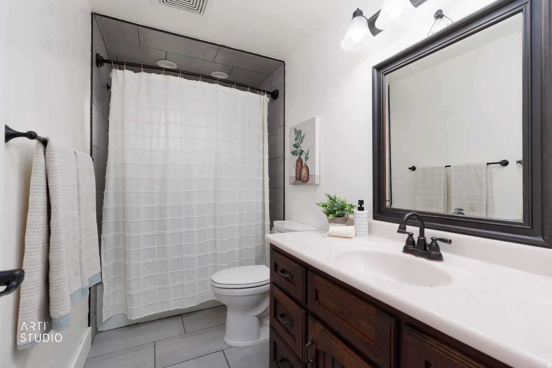 Bathroom featuring a dark wood-finish vanity with an integrated white sink, a framed mirror, and dark tile shower walls