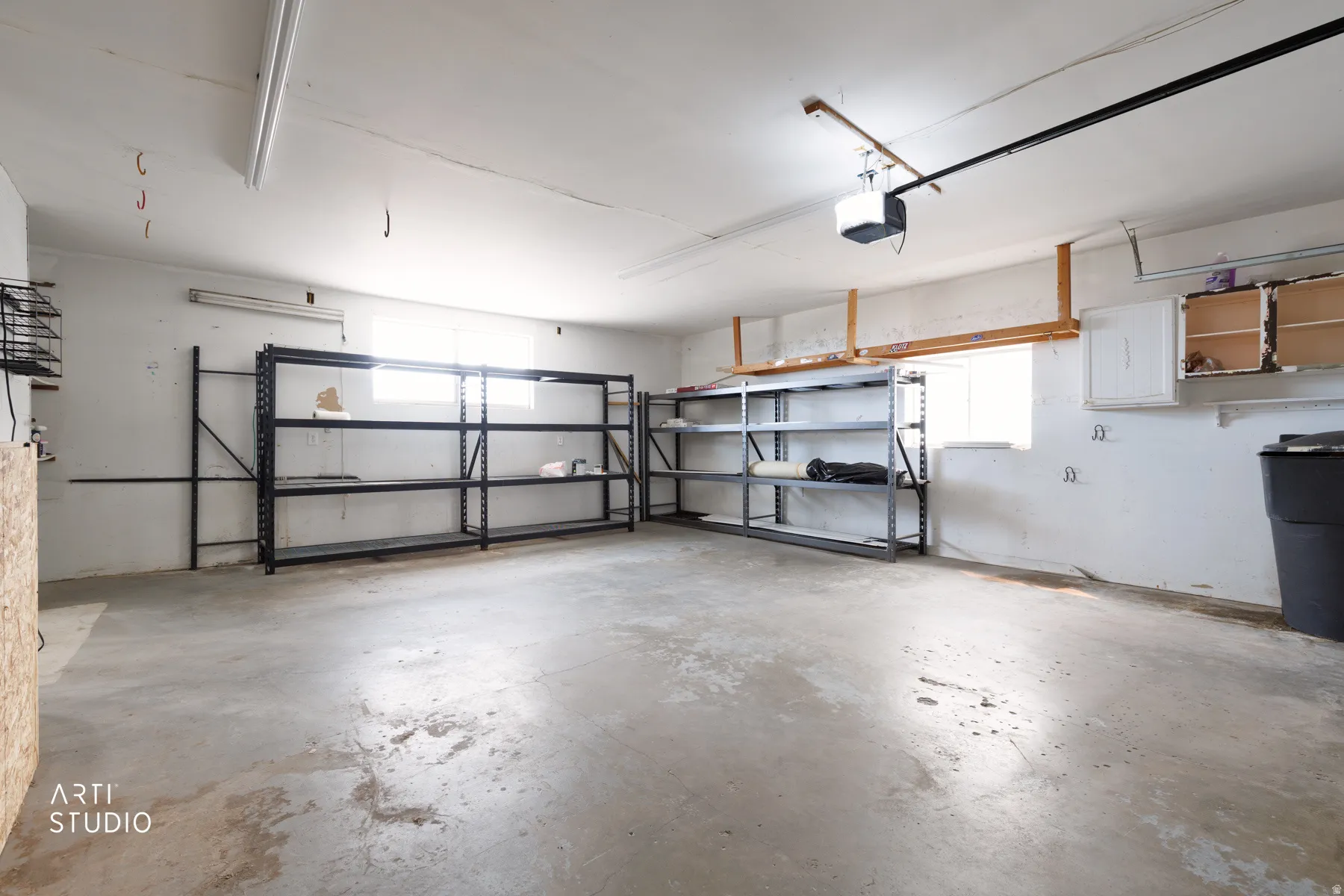 Spacious garage featuring a concrete floor, high ceilings, built-in shelving, a garage door opener, and a window for natural light