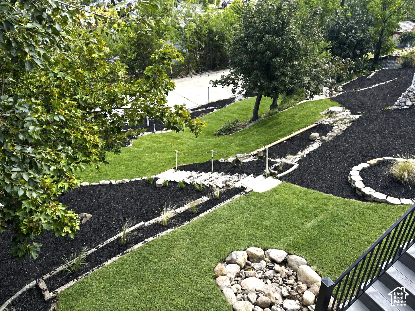 Tiered landscaping with expansive green lawn, natural stone steps, and decorative rock features