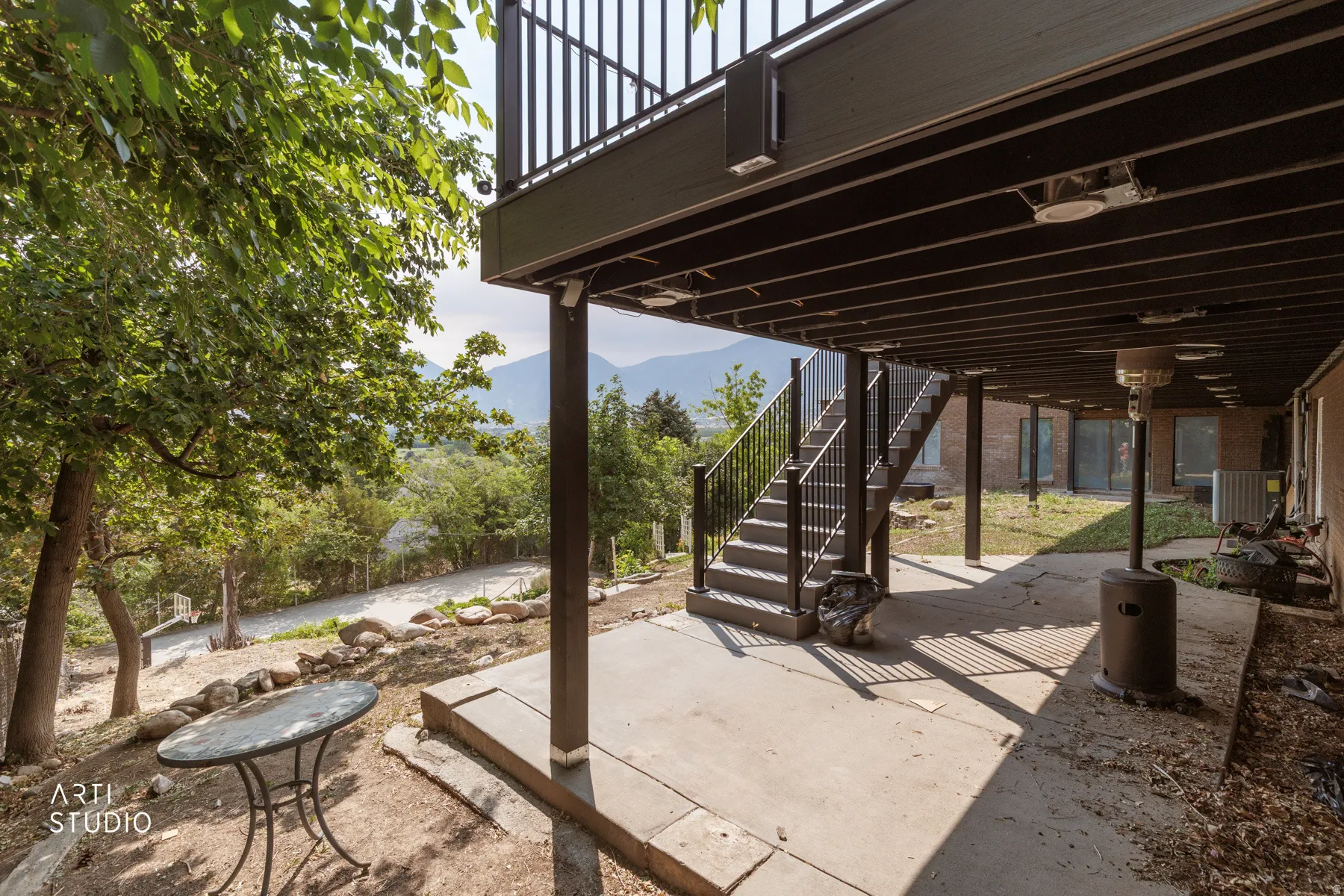 Lower-level concrete patio with an overhead deck, offering a shaded outdoor space