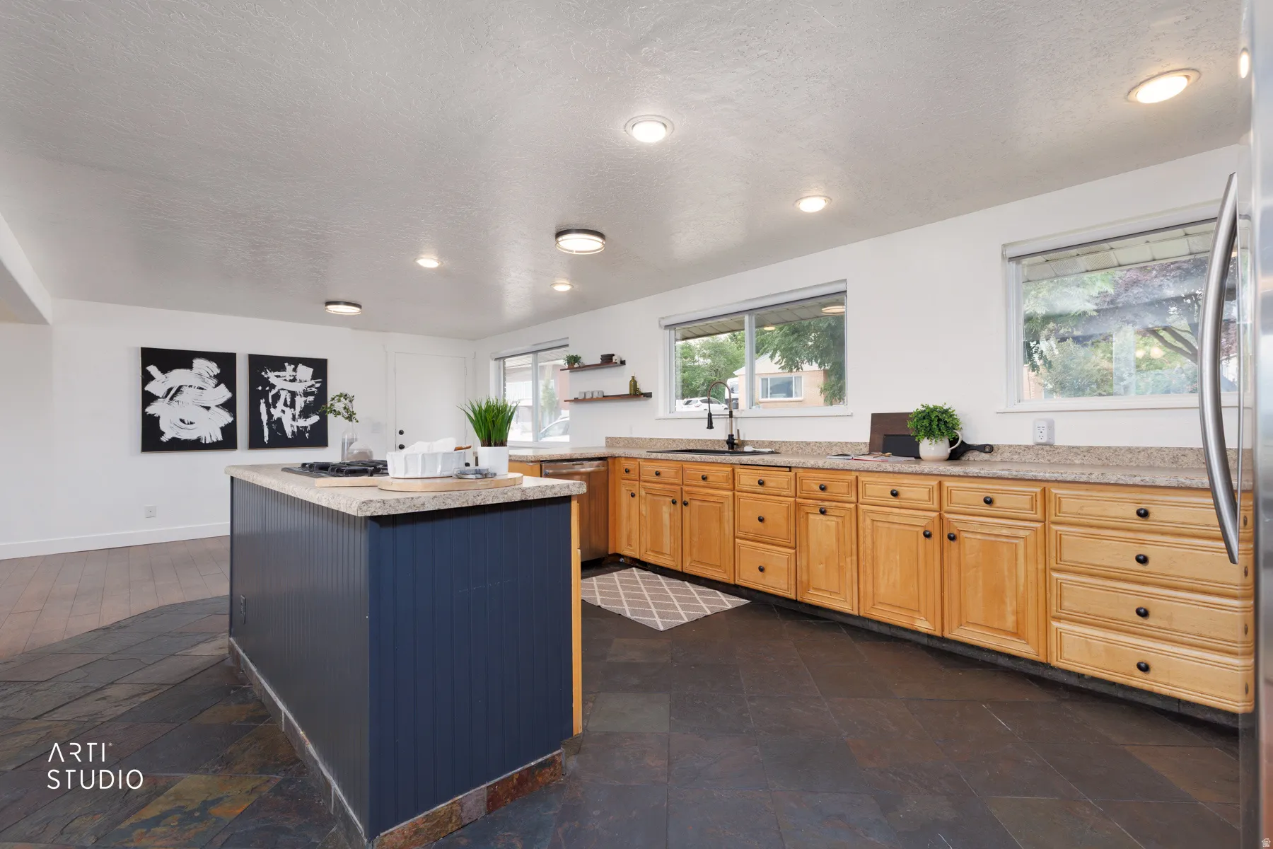 Kitchen featuring a large central island with beadboard paneling, light-colored countertops, wood cabinetry with black hardware, and dark slate flooring