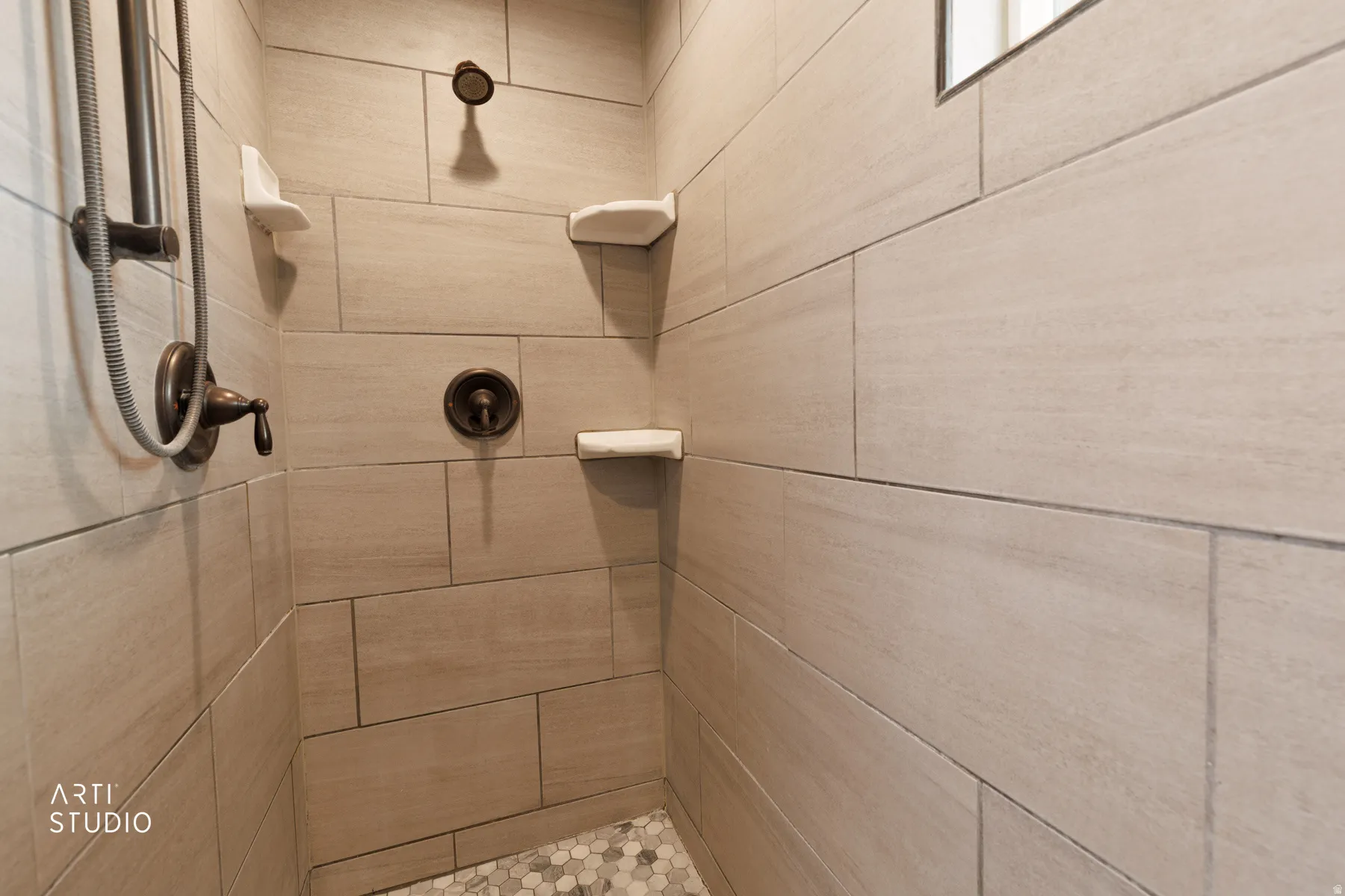 Shower stall featuring large format rectangular wall tiles, a mosaic tile floor, and oil-rubbed bronze fixtures, including a handheld showerhead