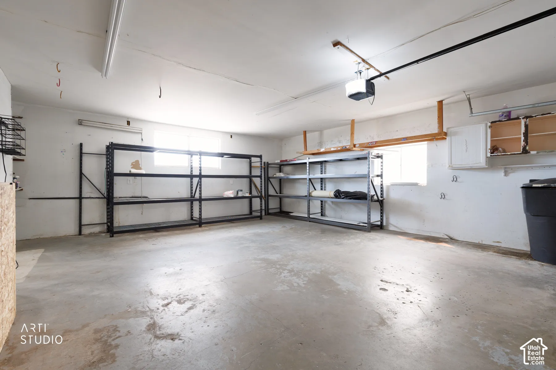 Spacious garage featuring a concrete floor, high ceilings, built-in shelving, a garage door opener, and a window for natural light