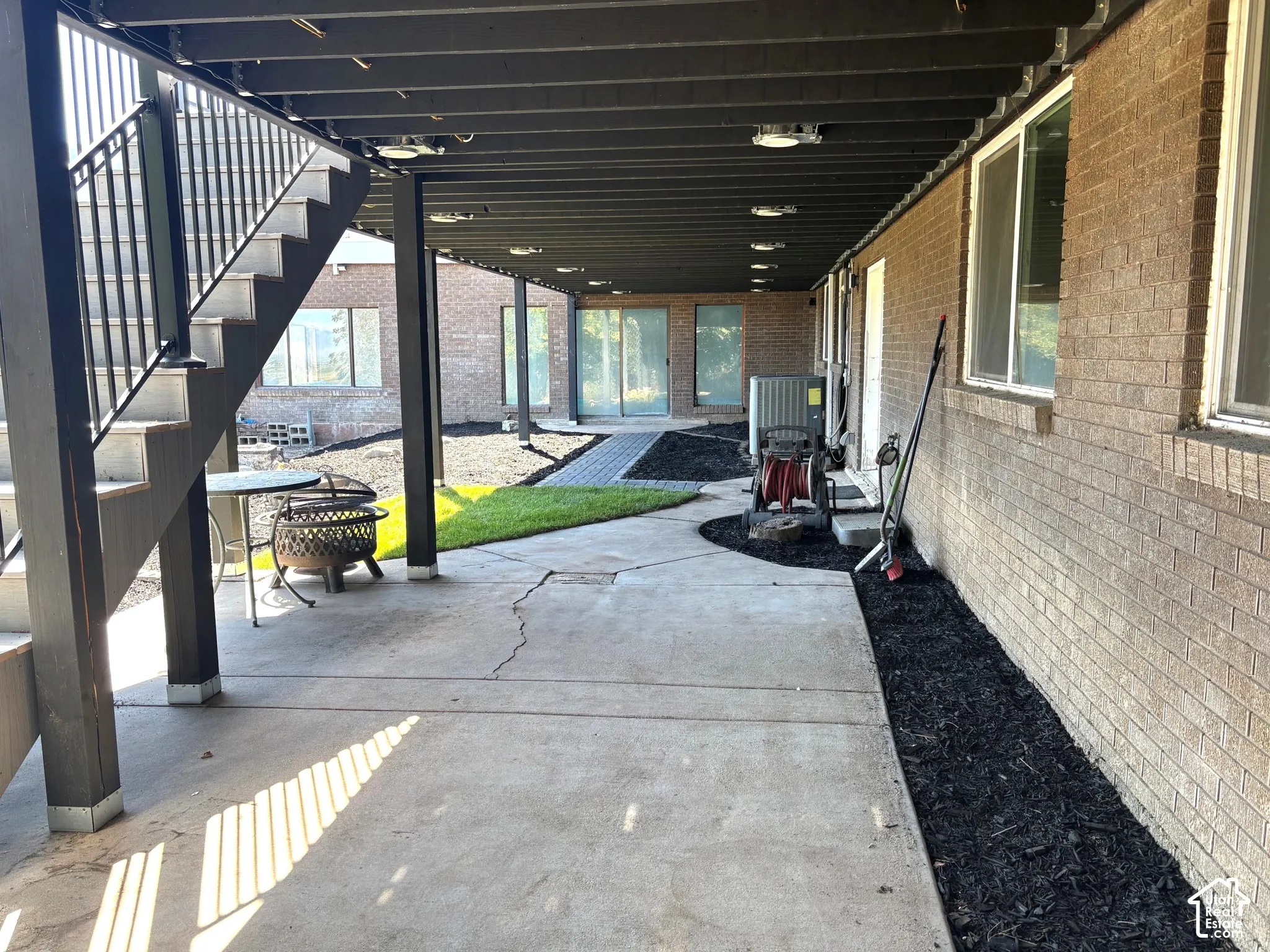 Concrete patio with overhead lighting, brick exterior, and landscaped beds with dark mulch