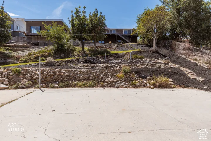 Concrete pad, tiered landscaping, stone retaining walls, and mature trees