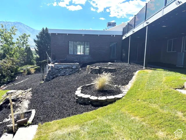 Terraced landscaping with dark mulch, stone retaining walls, a grassy lower level, and a multi-level deck above