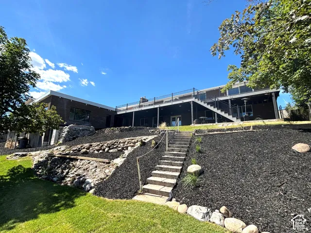 Tiered landscaping with stone steps, a expansive deck with metal railings, and a lower-level patio