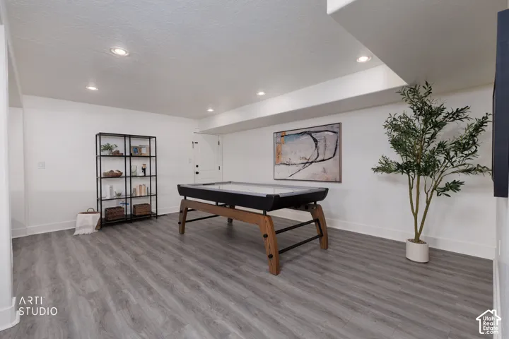 Spacious recreation area featuring wood-finish flooring, white walls, and recessed lighting
