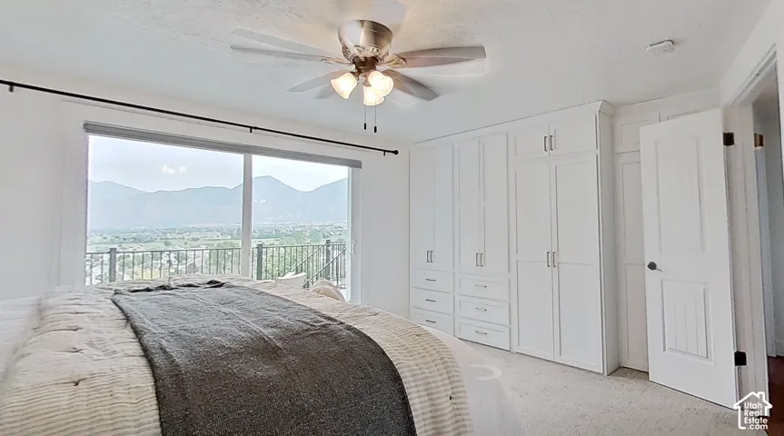 Room featuring a sliding glass door, a balcony with metal railings, a ceiling fan, white built-in cabinetry with silver-tone hardware, and light-toned carpet flooring