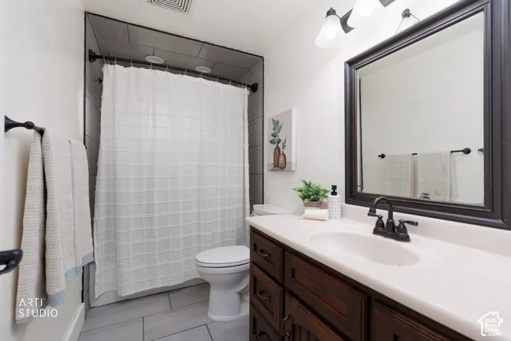 Bathroom featuring a dark wood-finish vanity with an integrated white sink, a framed mirror, and dark tile shower walls