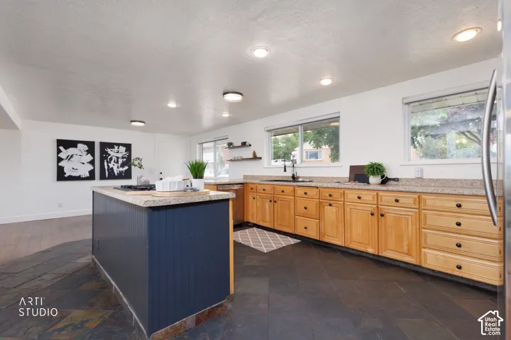 Kitchen featuring a large central island with beadboard paneling, light-colored countertops, wood cabinetry with black hardware, and dark slate flooring