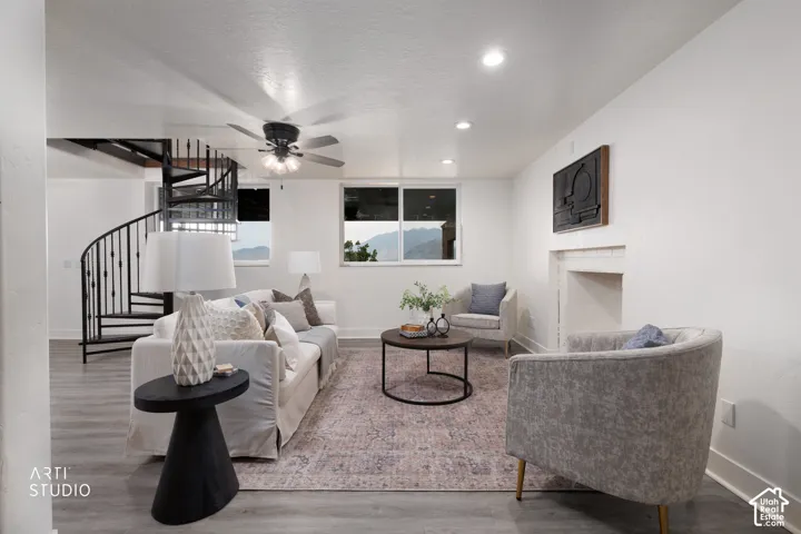 Living space featuring wood-finish flooring, a spiral staircase with metal balusters, a ceiling fan with integrated lighting, recessed lighting, and a fireplace