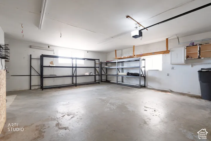 Spacious garage featuring a concrete floor, high ceilings, built-in shelving, a garage door opener, and a window for natural light