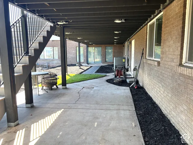 Concrete patio with overhead lighting, brick exterior, and landscaped beds with dark mulch
