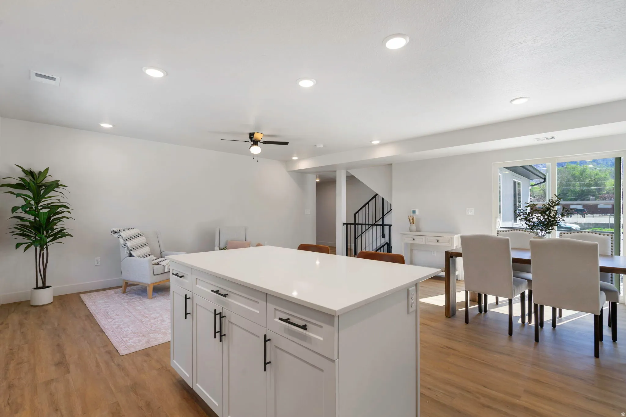 Spacious interior featuring wood-finish flooring, a kitchen island with a light-toned countertop, recessed ceiling lighting, a ceiling fan, and sliding glass doors