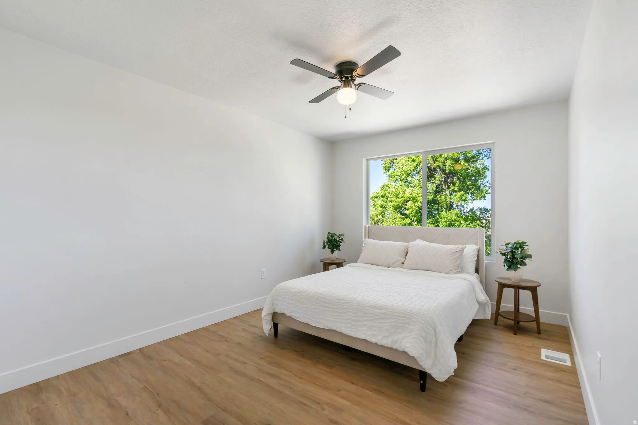 Spacious room featuring wood-finish flooring, white walls, and a ceiling fan with integrated lighting