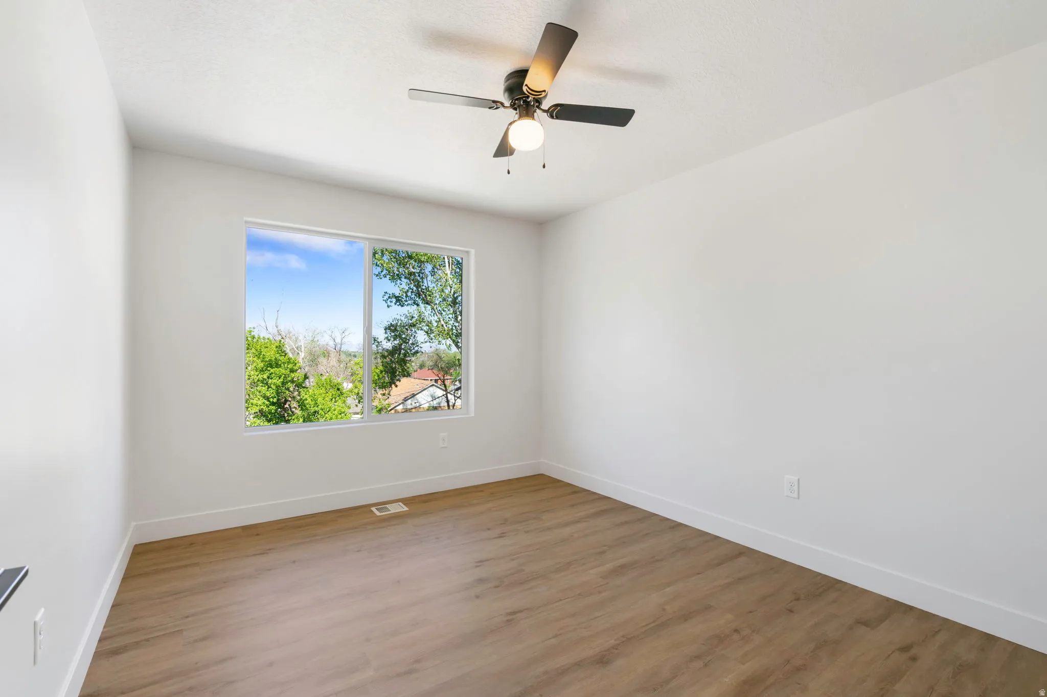 Bright interior space featuring a large window, wood-finish flooring, white walls, and a ceiling fan with integrated lighting