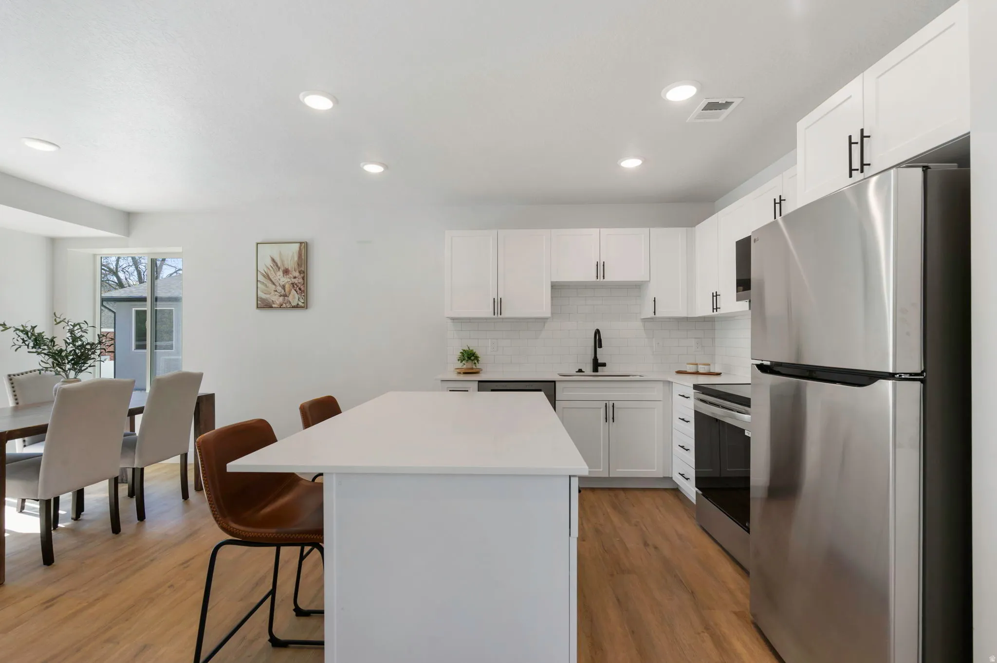Modern kitchen featuring white cabinetry, stainless steel appliances, a white subway tile backsplash, and wood-finish flooring