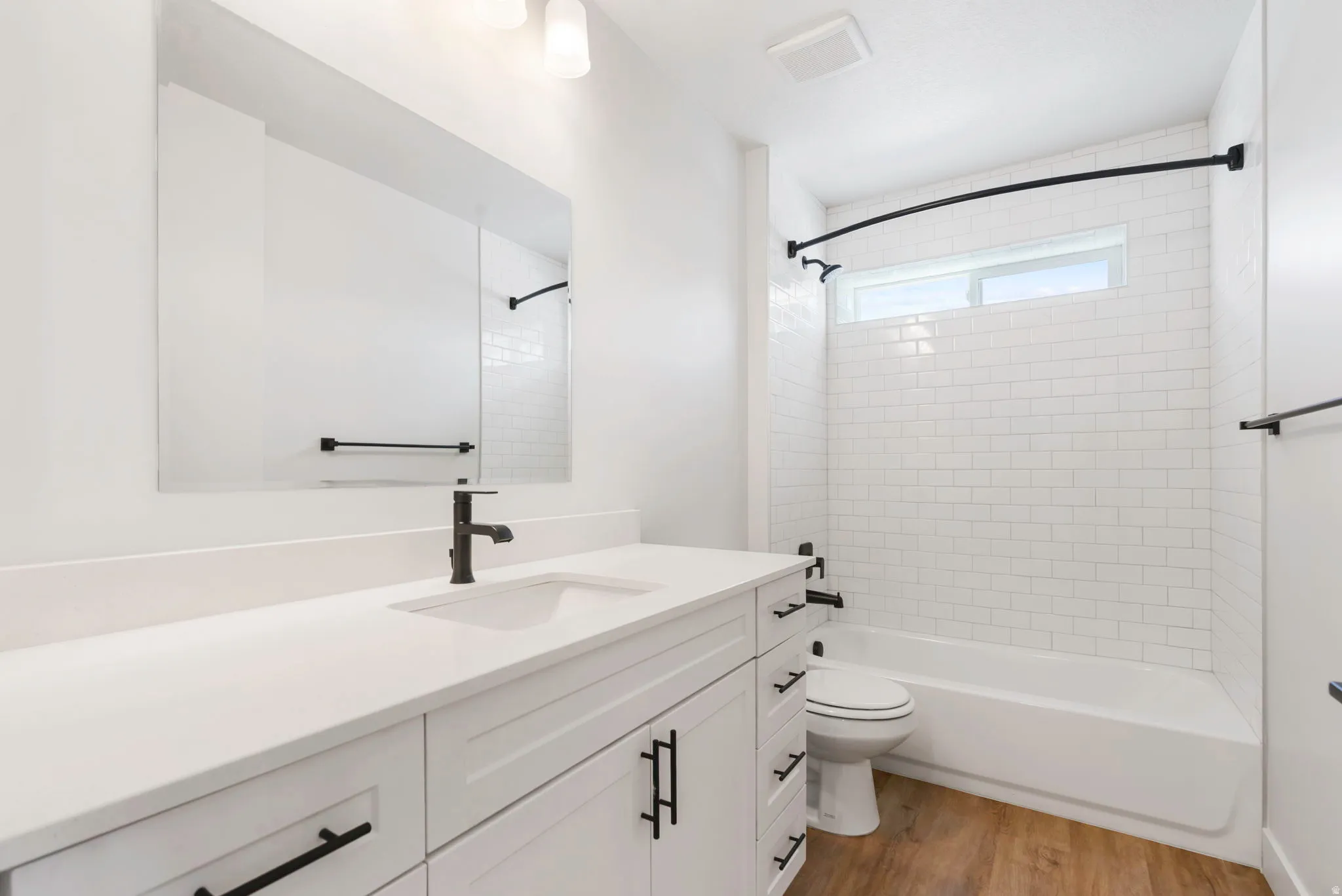 Bathroom featuring a white subway tile shower surround with a fixed window, a white bathtub, and matte black fixtures
