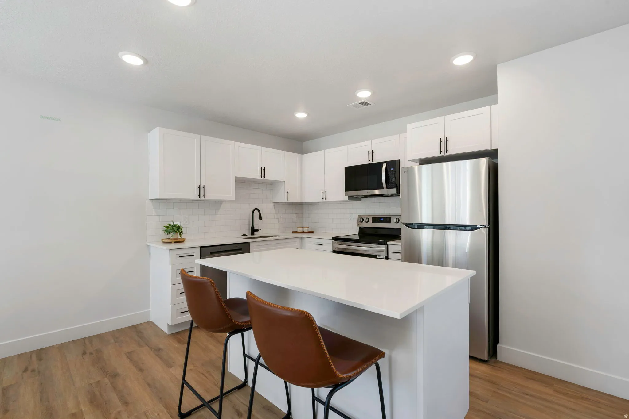 Modern kitchen featuring white cabinetry, a white subway tile backsplash, stainless steel appliances, a center island with countertop seating, and wood-finish flooring