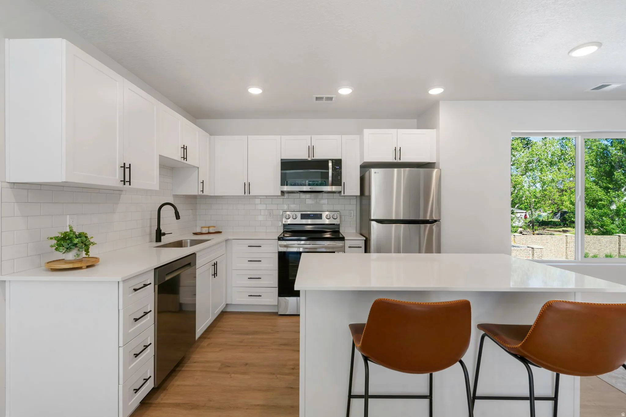 Modern kitchen featuring white cabinetry with matte black hardware, white subway tile backsplash, stainless steel appliances, and a central island with a solid surface countertop