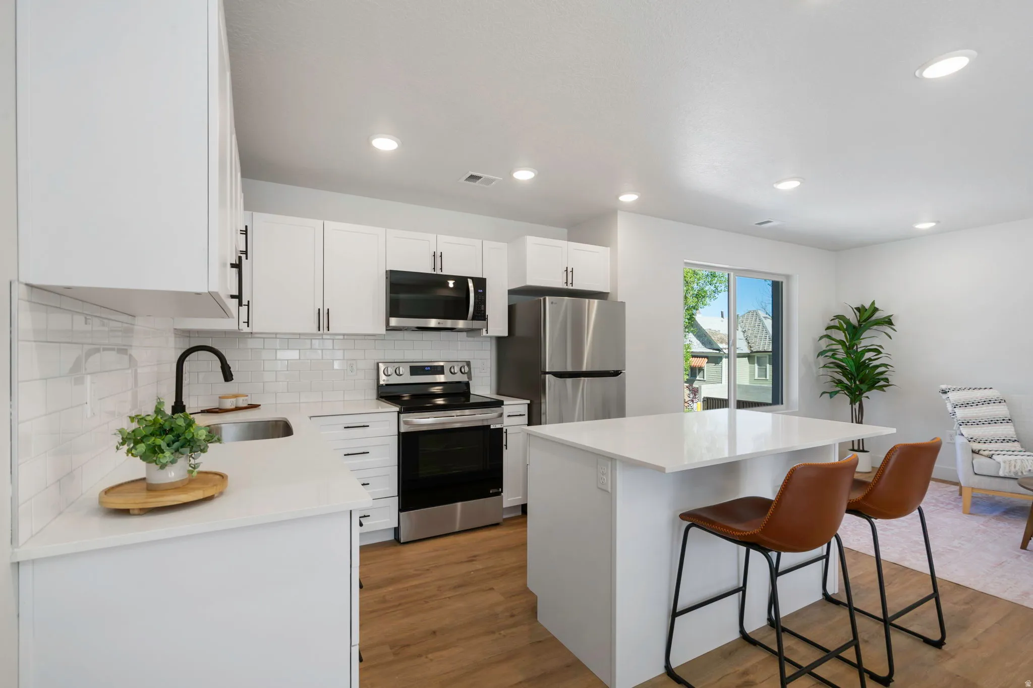 Modern kitchen featuring white cabinetry with black hardware, stainless steel appliances, a white subway tile backsplash, and light wood-finish flooring
