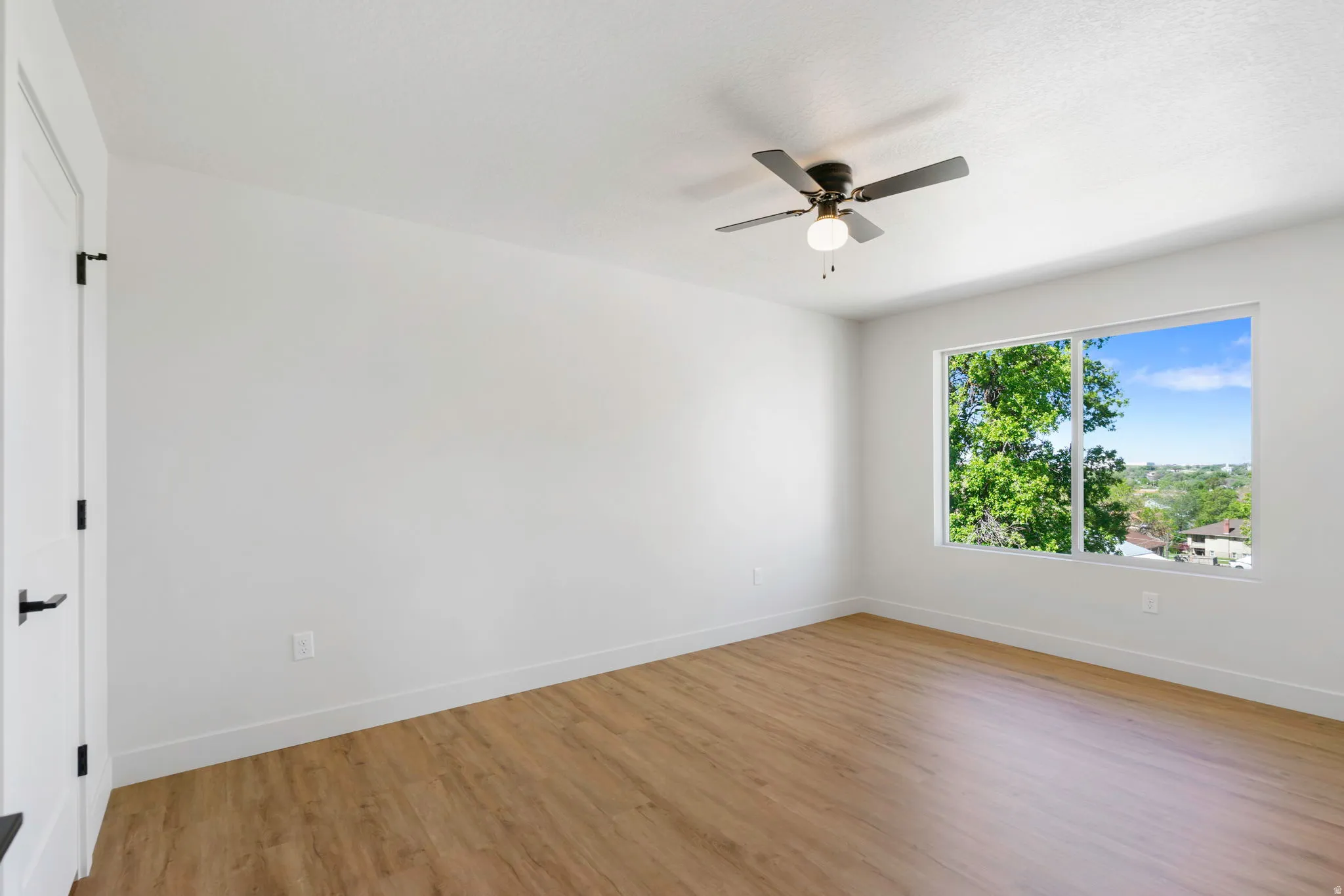 Bright room featuring a large window, wood-finish flooring, white walls, and a ceiling fan with integrated lighting