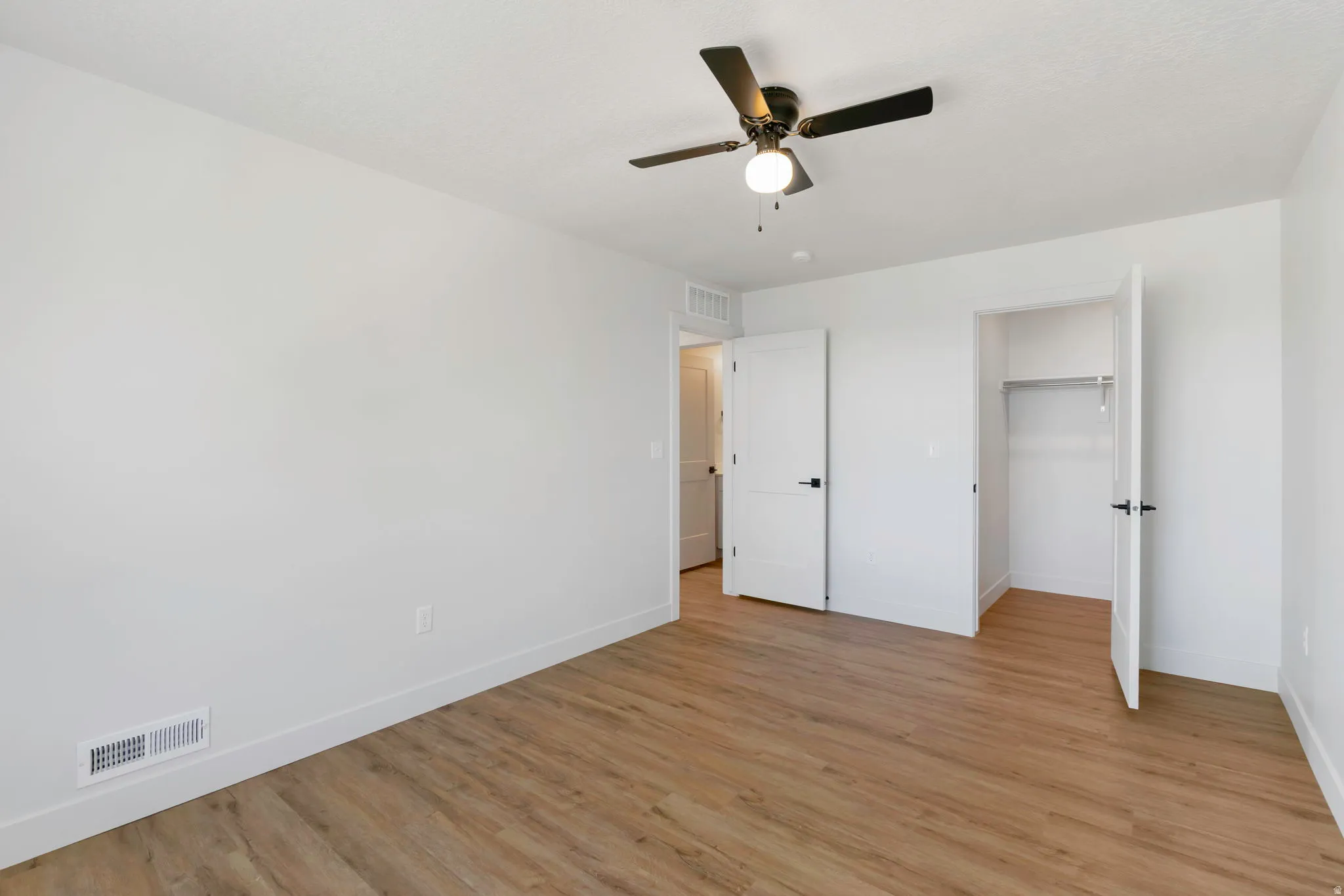 Bright room featuring wood-finish flooring, white baseboards, and a black ceiling fan with integrated lighting