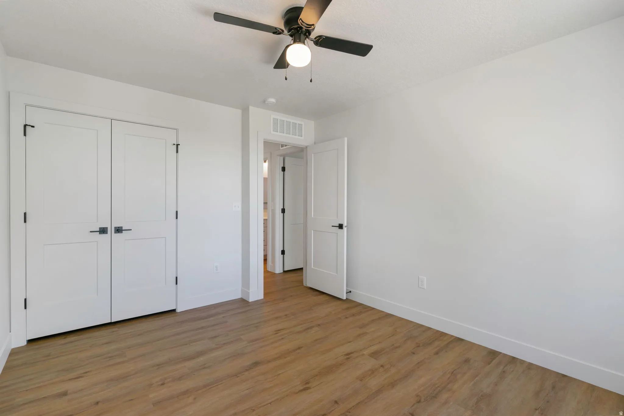 Room featuring wood-finish flooring, white walls, a ceiling fan, and white doors with matte black hardware