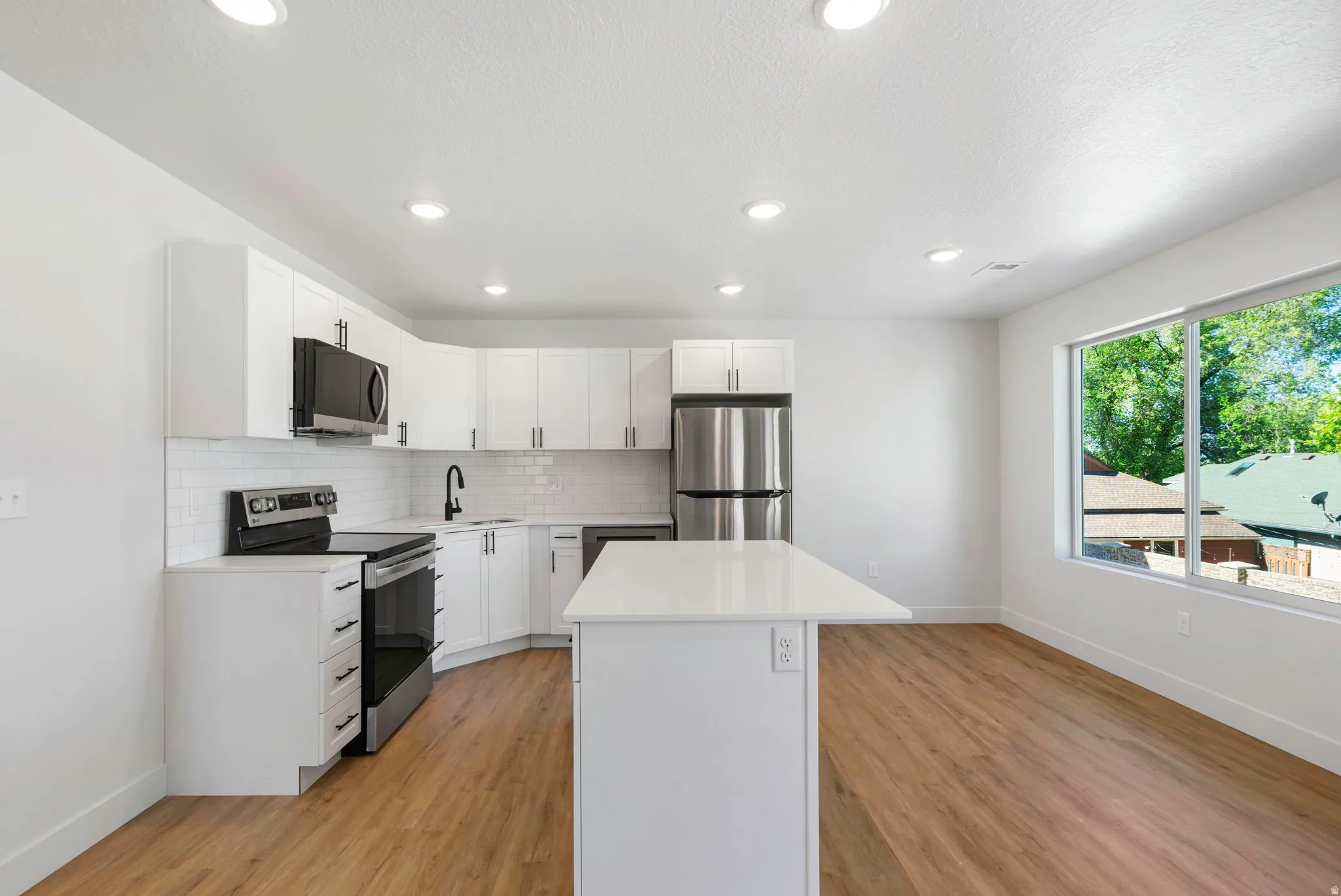 Bright kitchen featuring white cabinetry, a white subway tile backsplash, and stainless steel appliances