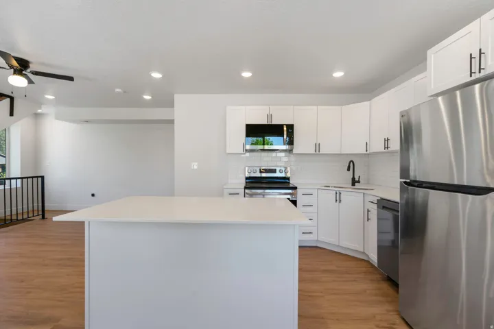 Modern kitchen featuring white cabinetry, stainless steel appliances, a white subway tile backsplash, and a large island with a light-toned countertop