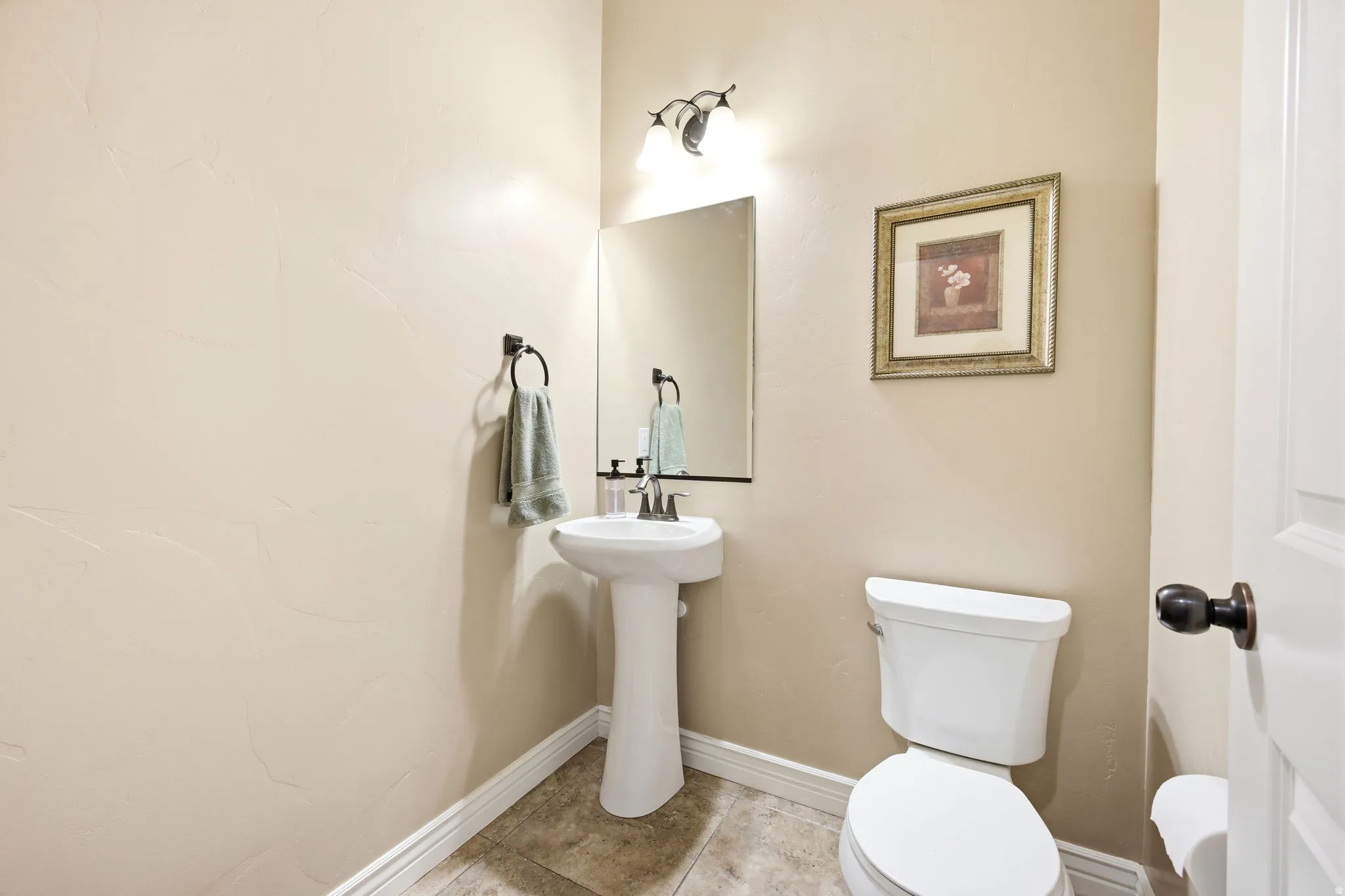 Pedestal sink with a wall-mounted mirror and overhead vanity lighting
