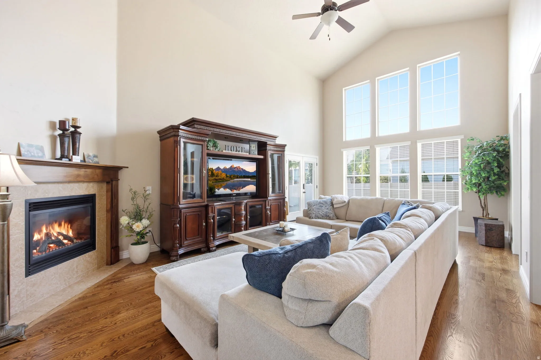 Vaulted ceiling living area featuring a corner fireplace with a wood mantle, wood-finish flooring, and a large window array